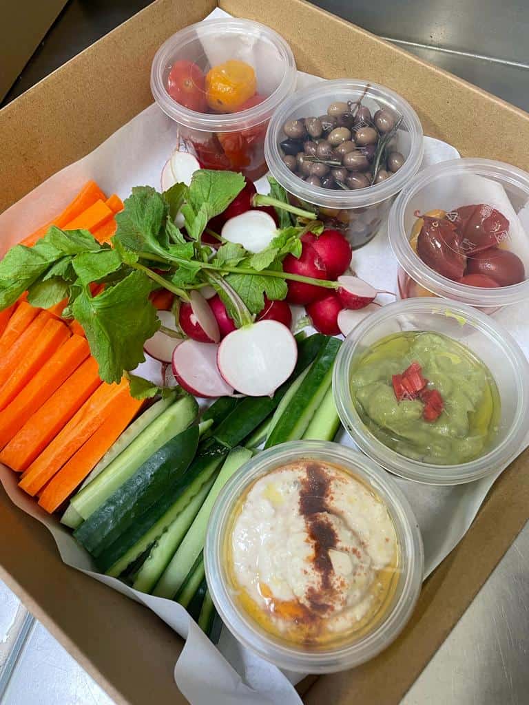 Colorful vegetable platter with hummus, olives, cherry tomatoes, and radishes for healthy snacking.