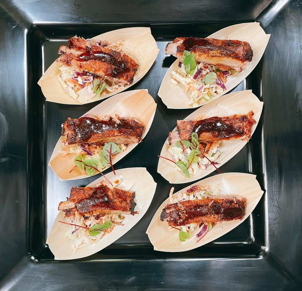 Delicious pork belly tacos topped with crispy pork, fresh coleslaw, and herbs, served on a black tray for an authentic meat experience.