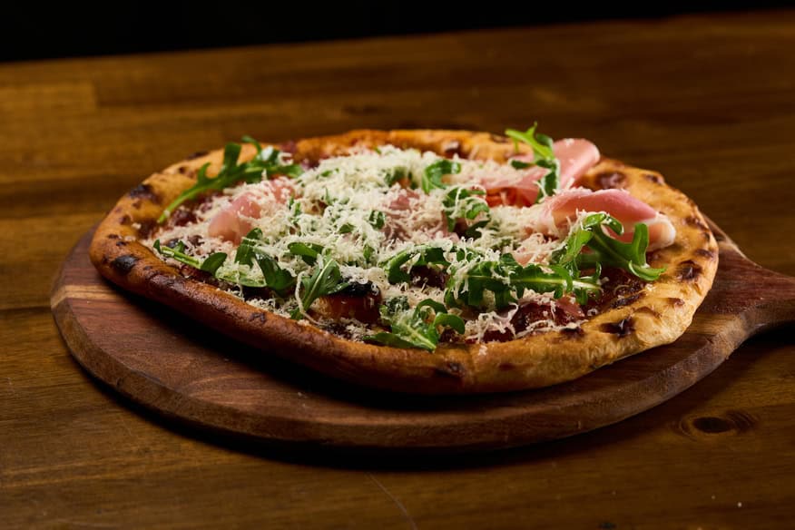 Delicious gourmet pizza with ham, arugula, and cheese, perfect for meat lovers.
